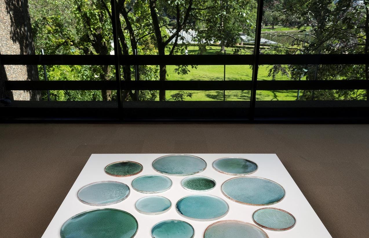 Bilder fra utstillingen Materielle påstander av Nina Malterud. Her ser vi et stort lavt bord med en mengde fat i ulik størrelse men samme sirulære form satt sammen i en gruppe.